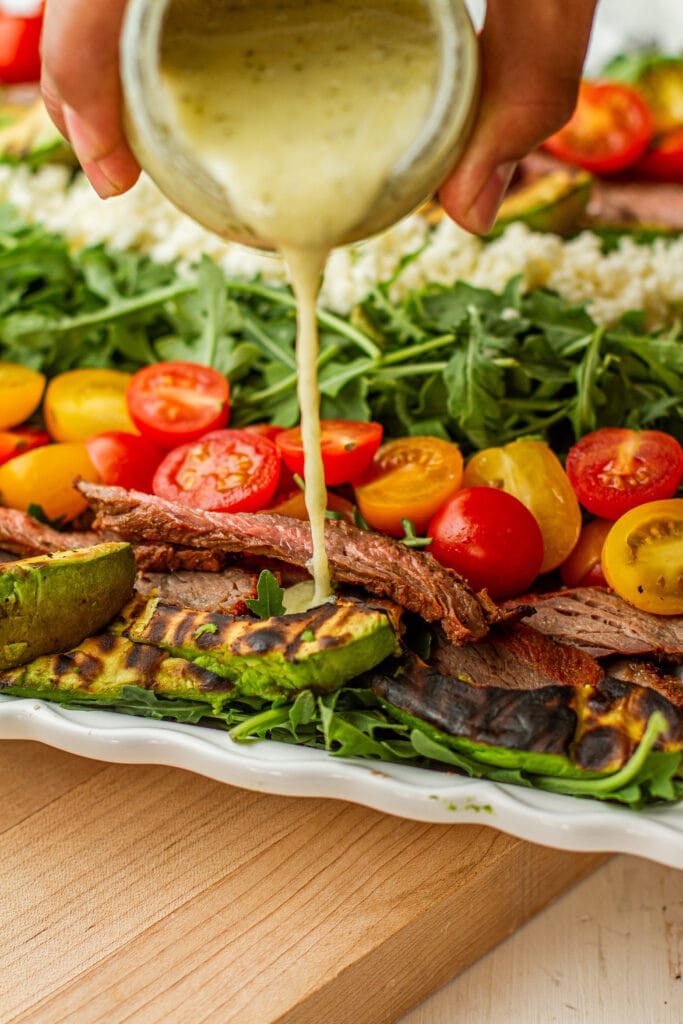 Grilled Avocado & Carne Asada Salad a platter while pouring dressing 