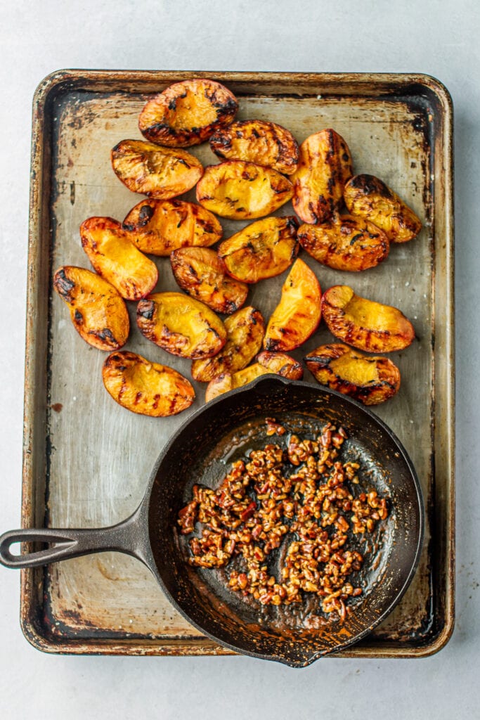 grilled peaches and Spiced Honey Pecans in a cast iron skillet on a baking sheet