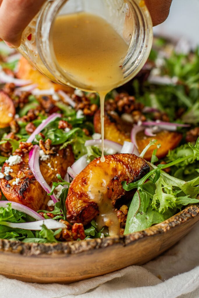 Grilled Peach Salad with Goat Cheese in bowl drizzling Lemon Honey Vinaigrette