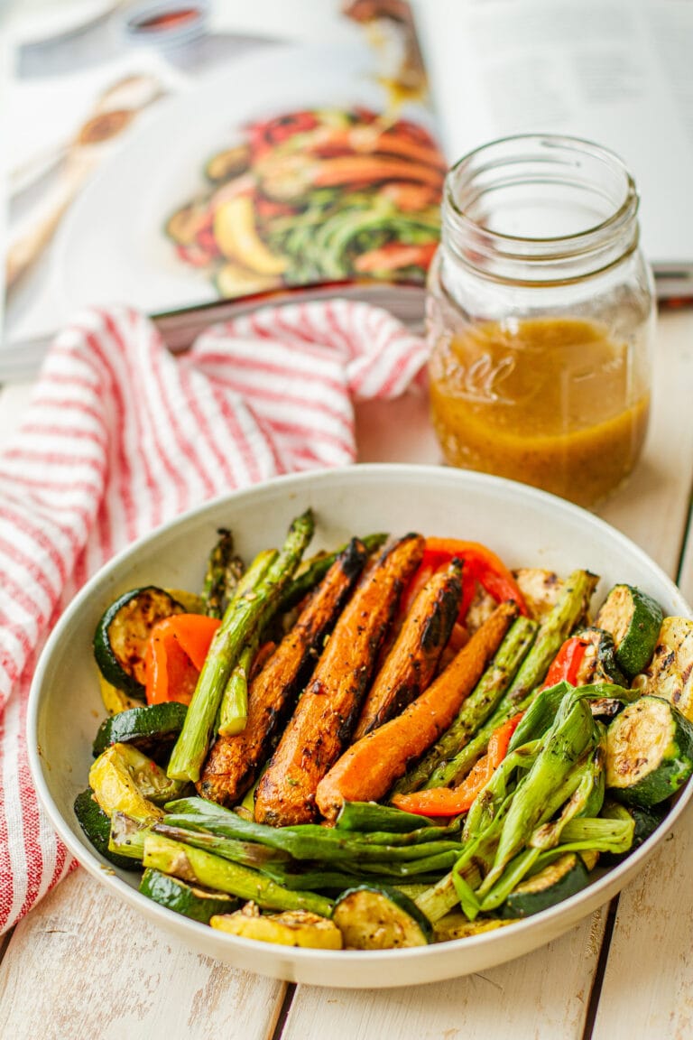 Rodney Scott’s Grilled Vegetable Salad in a white glass dish on a table next to dressing in a open mason jar