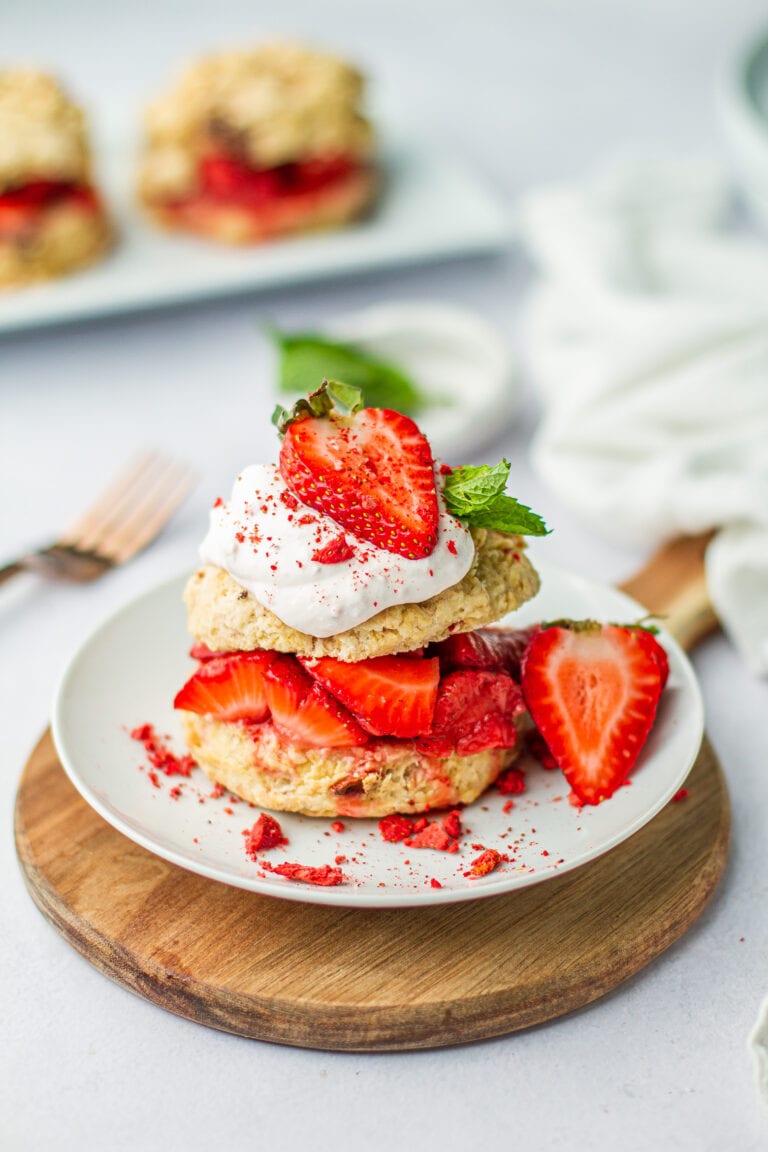 A plated portion of Very Strawberry Shortcake on a circle wooden cutting board on a white table