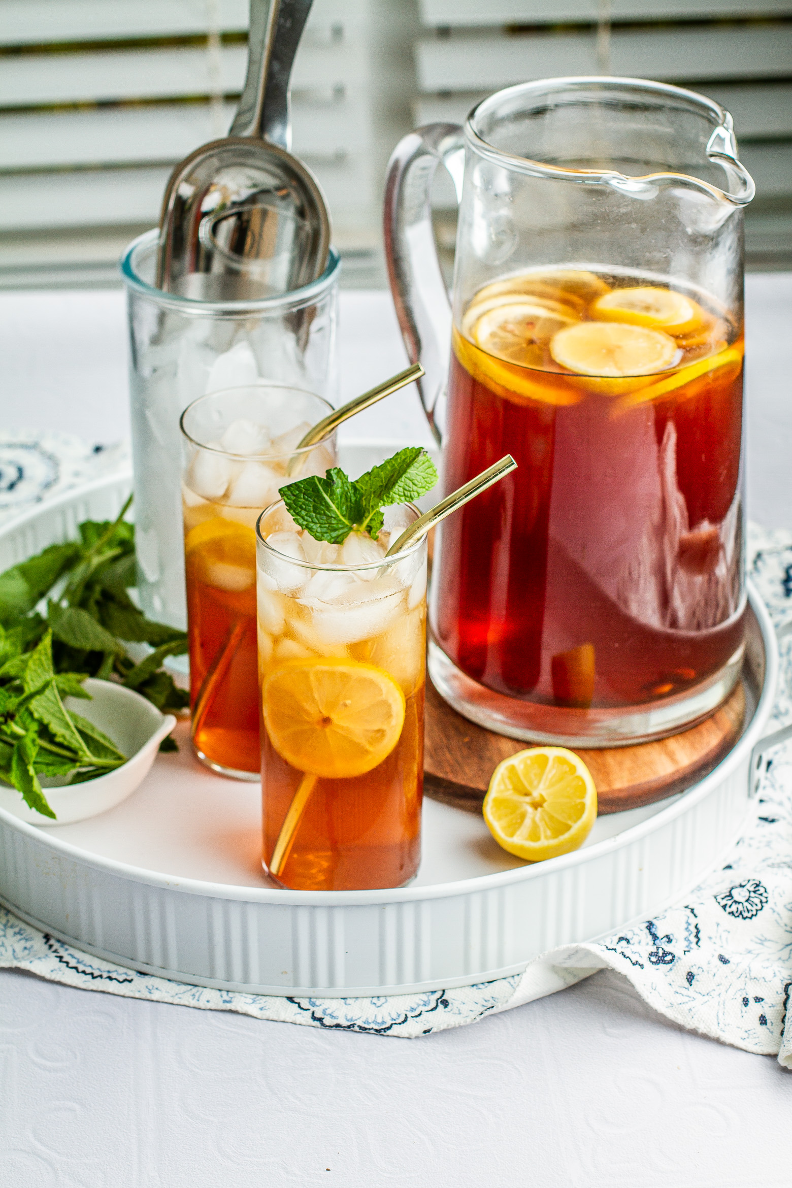 Southern sweet tea in a pitcher and two glasses on a serving tray garnish with mint and lemon