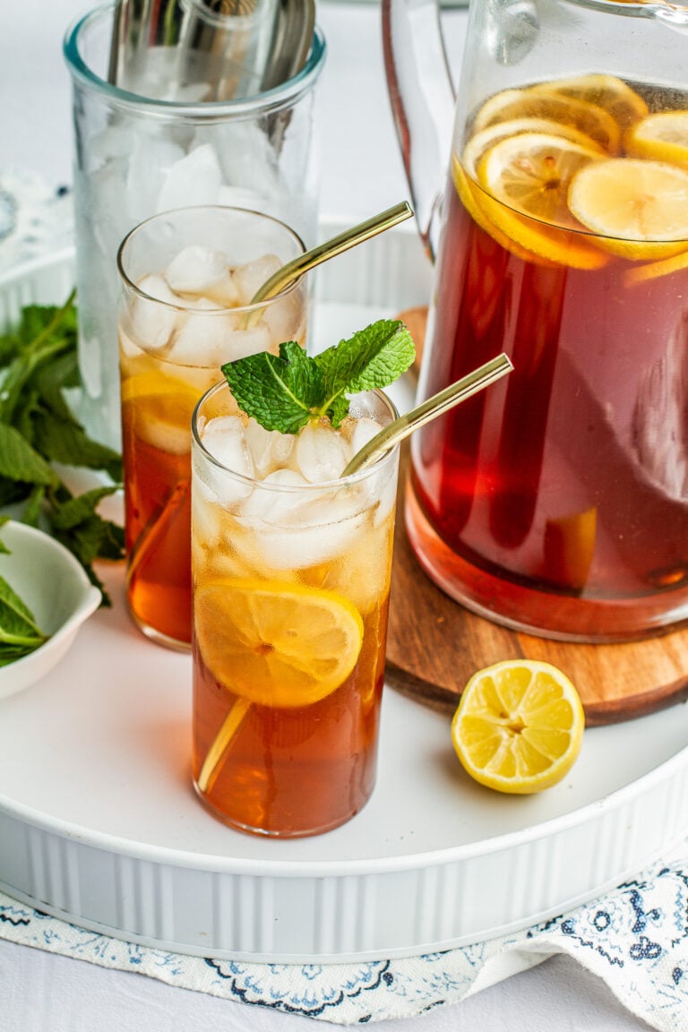 Southern sweet tea in a pitcher and two glasses on a serving tray garnish with mint and lemon