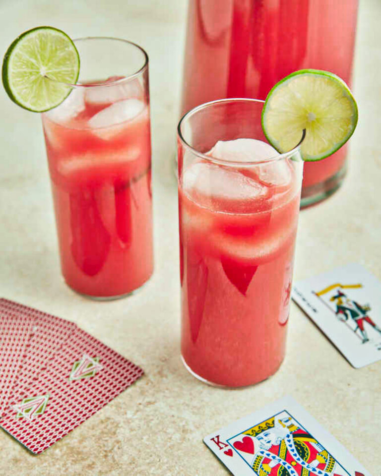 Overhead of watermelon limeade in a pitcher and in two glasses that decorated witha lime and playing cards