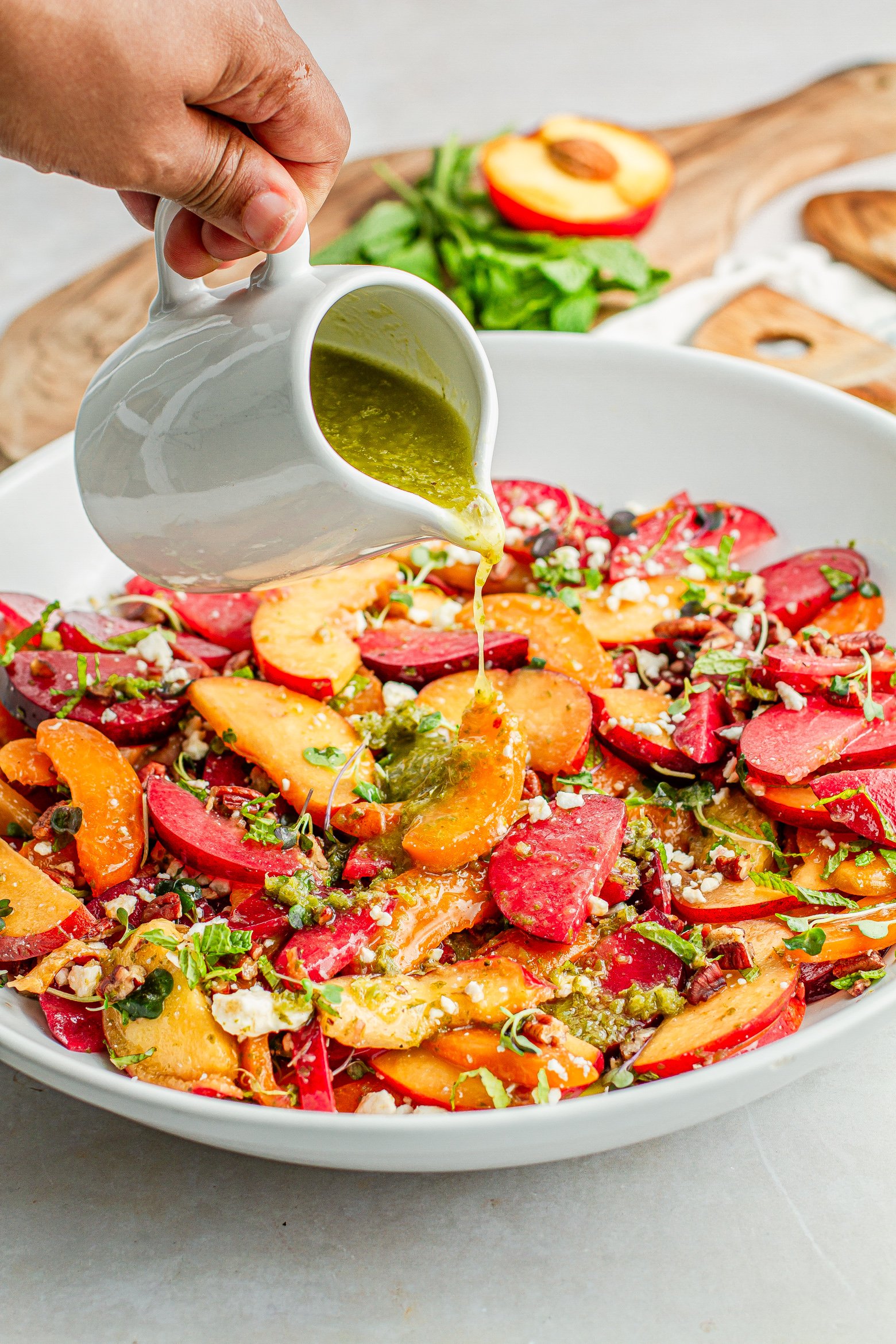 close up of drizzling dressing on Stone fruit salad on a platter